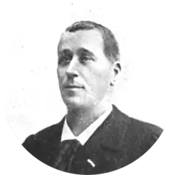 middle-aged white man, clean-shaven, with full head of neat dark hair; he is dressed in day clothes, with collar and tie