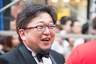 A smiling, bespectacled Shinji Higuchi at a formal event