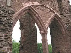 Part of a castle, with a huge semi-circular arch containing two smaller Norman arches dominating the picture. Through the arches, a ruined pillar can just be made out.
