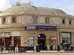A beige-bricked building with a blue sign reading "GREAT PORTLAND STREET STATION" in white letters all under a blue sky with white clouds