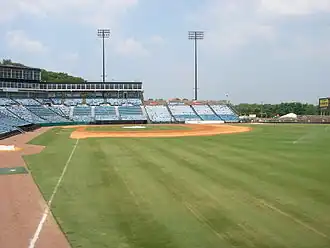 A view from right field shows the green grass and infield dirt of a baseball diamond surrounded by empty blue seats