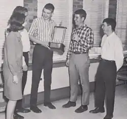 Photograph of high school debaters standing with a trophy