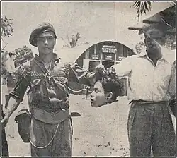 Commonwealth soldiers pose with a severed head inside a British military base in Malaya during the Malayan Emergency