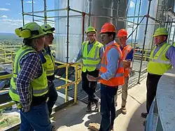 Several people in high-visibility vests and hard hats tour an industrial facility