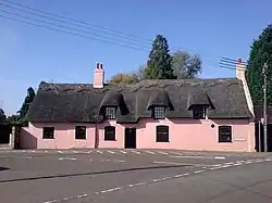Large pink thatched cottage built on slight curve of road 5 front windows 1 front door 3 attic windows chimney No front garden