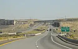 A divided highway approaching a dip in the road and an interchange near several apartment buildings