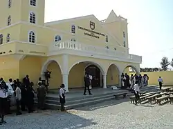 Congregants in their Sunday best outside of a yellow building bearing the church's name