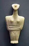 Marble figurine: most of its features are schematic, except a prominent nose, two breasts, and folded arms.