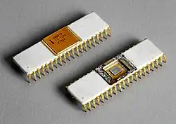 Close up of two small white rectangular microprocessor chips with small gold-colored metallic prongs extending from the side downward. The top left chip has a gold covering on the top middle portion that reads "C8080B, ES 1274, KI984". The bottom right chip has the cover removed exposing the die of semiconducting material.