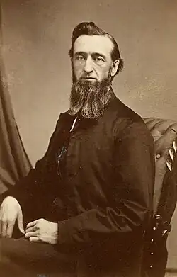 Portrait of a bearded man in a dark jacket sitting in a chair