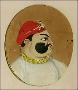 A color portrait of a mustached man, from the chest up, wearing a crown