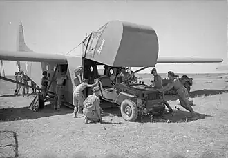Men pushing a jeep into a glider, which has the front cockpit raised to allow access