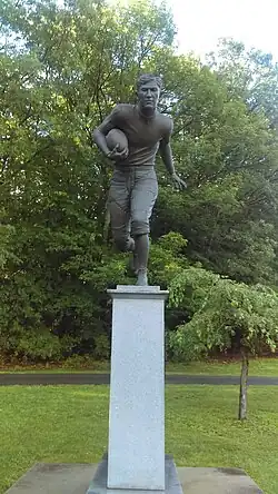 Statue of Jim Thorpe dashing while carrying a football in front of a group of trees