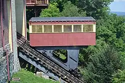 A side view of the Johnstown Inclined Plane. The car is painted red, with yellow windows. The track slopes down from top left to bottom right.