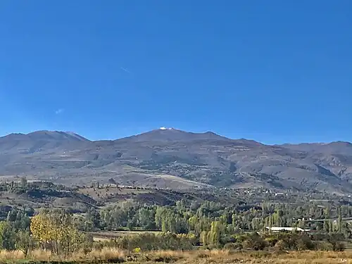 Photograph of a valley slope rising in the distance to a mountain range, with snow visible on one peak