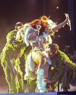 SZA about to be carried by backup dancers wearing grasslike draperies