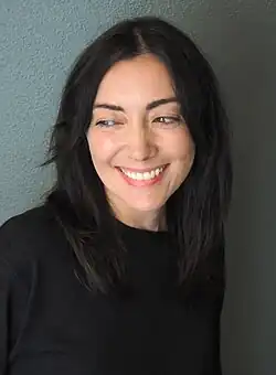 A photograph of Kerry Howley depicting her head and shoulders. She is wearing a black sweater, smiling broadly, and looking sideways.