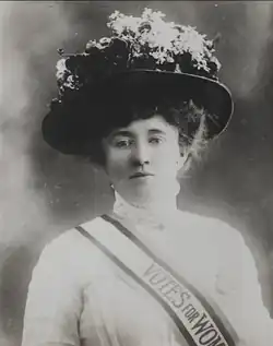 A black and white photograph of the head of a woman, looking at the viewer, in Victorian-era clothing