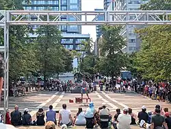A man in shorts juggles on a public place in front of a large crowd
