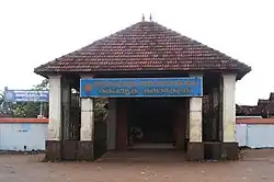 Entrance to low building with four white columns, triangular roof and blue sign