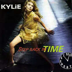 An image of a singer Kylie Minogue wearing a gold-like dress, and standing in front of a blue-ish white background with lights. The song title, a backwards clock, and the name is superimposed on the cover.