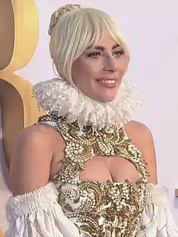 Lady Gaga smiling and wearing a golden outfit.