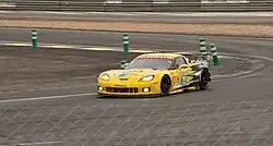 A photograph of a yellow and black grand touring racing vehicle exiting a racing circuit corner
