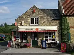 Stonebuilt shop with modern PVC folding canopy, on a sunny day. A bright pot of flowers on the left, and ivy up the stone building on the right.
