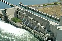 Detail view of a portion of a concrete dam, showing a fish ladder in between a spillway to the left and a navigation lock to the right.
