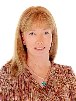 Lynn Conway in front of a white background. She is a middle-aged white woman with reddish blonde hair, wearing a colorful .