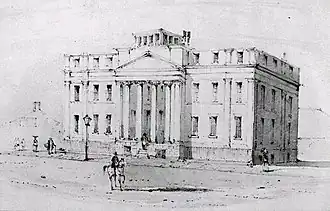 Black and white drawing of a large three-storey building fronted by a four-column portico. A man on a light-coloured horse is riding down the wide empty street in front of the building.