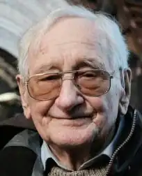 Colour Press headshot of a smiling, bespectacled, clean-shaven, elderly man with white hair