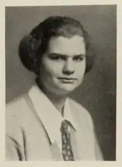 A young woman in a collared shirt and tie, with a neutral expression