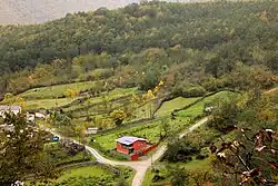A photograph taken from a height shows a rural area with small fields and houses connected by dirt roads.