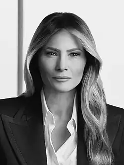 Official portrait of Melania Trump, a middle-aged white woman with long dark hair, wearing a black suit.