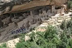 a group of people observing Indian ruins located in a cave.