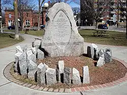 circular monument in a park, and made of multiple grey stones. The large central stone contains a bilingual inscription in memory of women killed by men's violence. Many much smaller irregularly shaped stone shafts are carved with women's names.