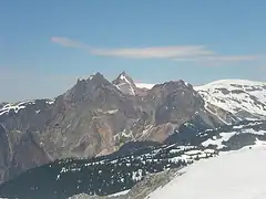 Mountain with three peaks rising above glaciated landscape in the background and above vegetation in the foreground.