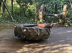 A large tyre on chains in a courtyard - a child's feet and legs poke out of the middle wearing gumboots. The evening sun is dappled.