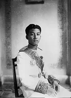 Sihanouk sitting in a wooden chair while dressed in a French military uniform in a black-and-white photograph