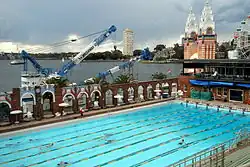 The 50 metre North Sydney Olympic Pool. The entrance to Luna Park and its Ferris Wheel is visible in the background. In front of Luna Park, a crane barge is on the harbour.