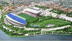 Aerial view of football field with parkland below and buildings to the right.