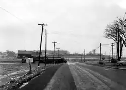 Black and white image of a two lane road travelling through muddy fields