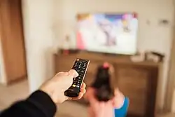 Parent using a remote control and young girl in front of a television in a blurry background