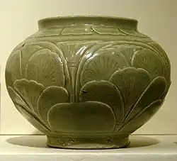 A green-grey bowl with a small bottom, a very wide center, and a top opening wider than the base but not as wide as the center. A pattern of out-dented large leaves covers the body of the bowl.