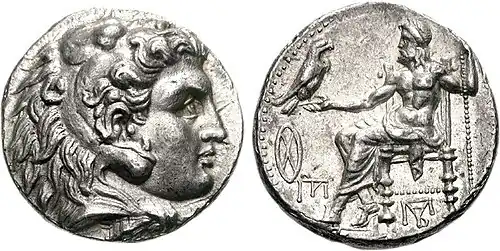 A color photograph of two silver coins against a white background, the front shows a long-haired man, the back shows a Greek god seated on a chair with a bird resting on his right hand