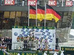 A group of drivers on a podium with three German flags raised above them