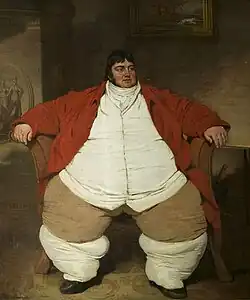 Smartly dressed fat man with dark hair and a red waistcoat, sitting on a chair