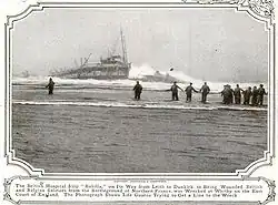 Black and white photo of a ship sinking into the water, with multiple people running towards it.