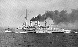 A large battleship plows through the water at high speed, thick black smoke pours from the smoke stacks